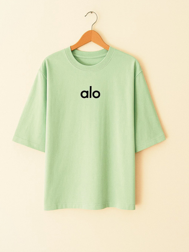 تیشرت زنانه سبز با طراحی ساده و نوشتهی کوچک alo روی سینه، استایل راحت و روزمره، آستینها تا آرنج، روی پسزمینه خنثی
