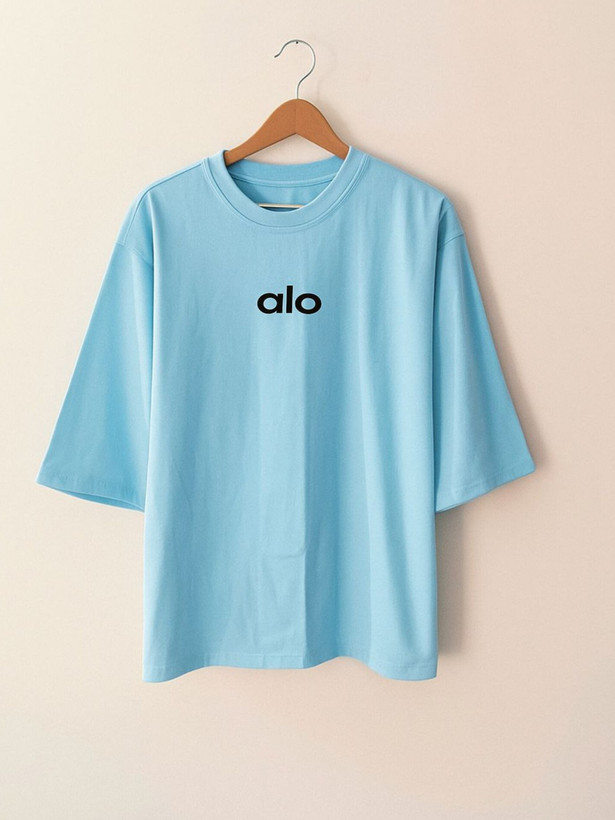 تیشرت زنانه آبی روشن با طراحی ساده و نوشته کوچک alo روی سینه، در ترکیب با آستینهای بلندتر ، حس خنکی و آرامش را به تصویر میکشد.