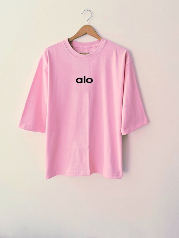 تیشرت زنانه صورتی روشن با نوشته کوچک alo روی سینه، طراحی مینیمال و آستینهایی تا آرنج، چیدهشده روی پسزمینه ساده
